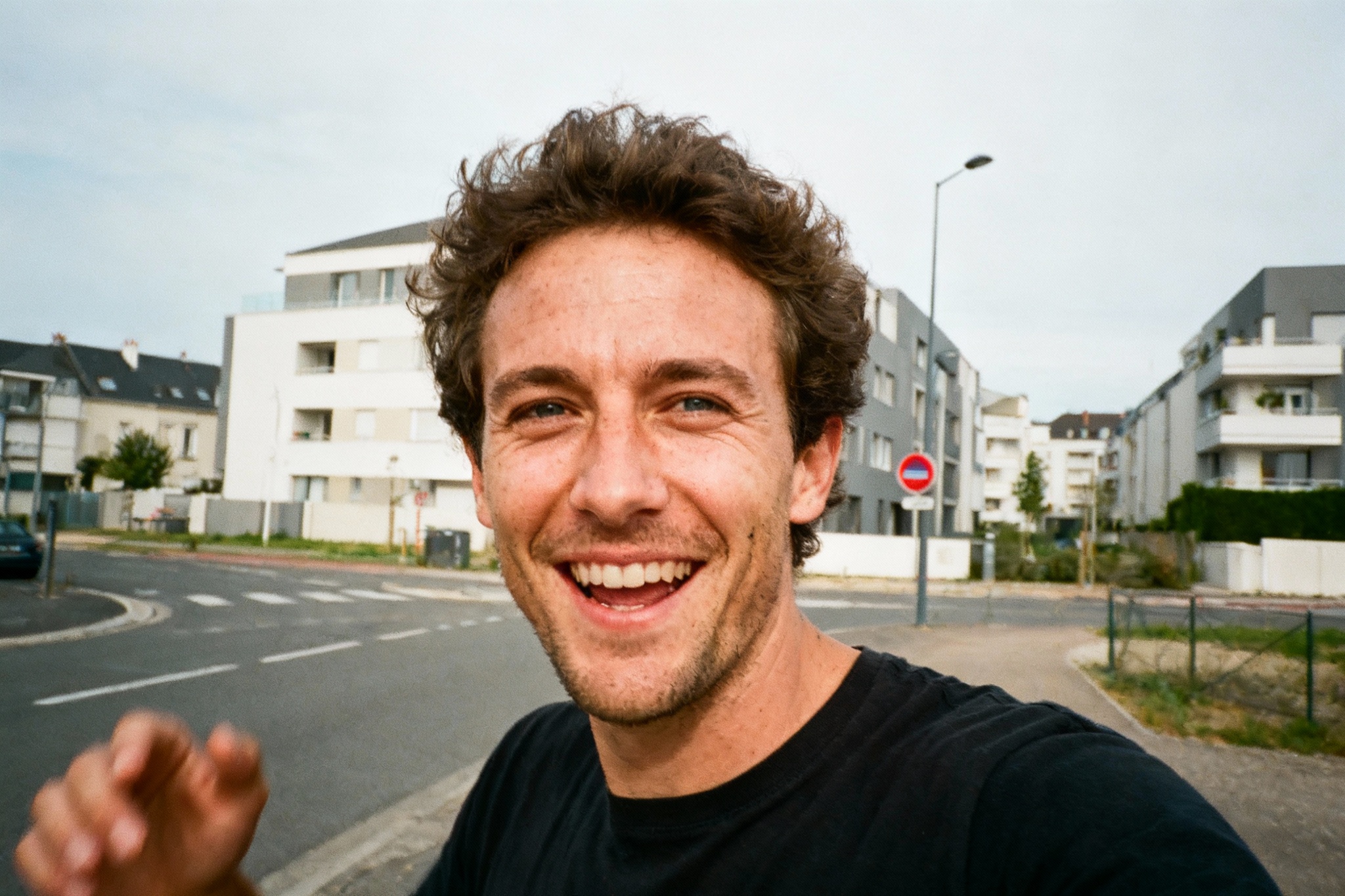 pexels-michal-pech-213601-757318 (1) Homme souriant à la caméra, avec des bâtiments modernes en arrière-plan et une route tracée au sol. Journée ensoleillée.