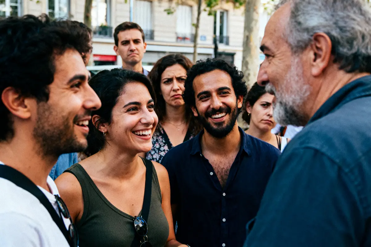 Un groupe de personnes discutant et souriant en extérieur, sur un trottoir urbain.