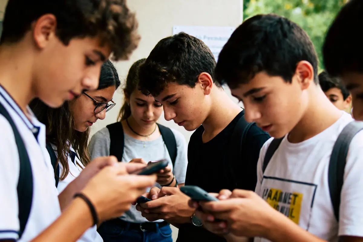 Adolescents concentrés sur leurs smartphones, en extérieur, portant des sacs à dos. Moment d'interaction digitale.