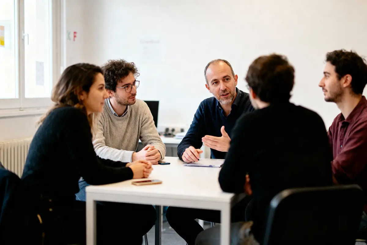 Cinq personnes discutent autour d'une table dans une salle de réunion lumineuse.
