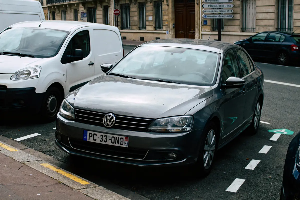 pexels-michal-pech-213601-757318 (1) Voiture Volkswagen grise stationnée à côté d'une camionnette blanche, rue urbaine avec panneaux de signalisation.