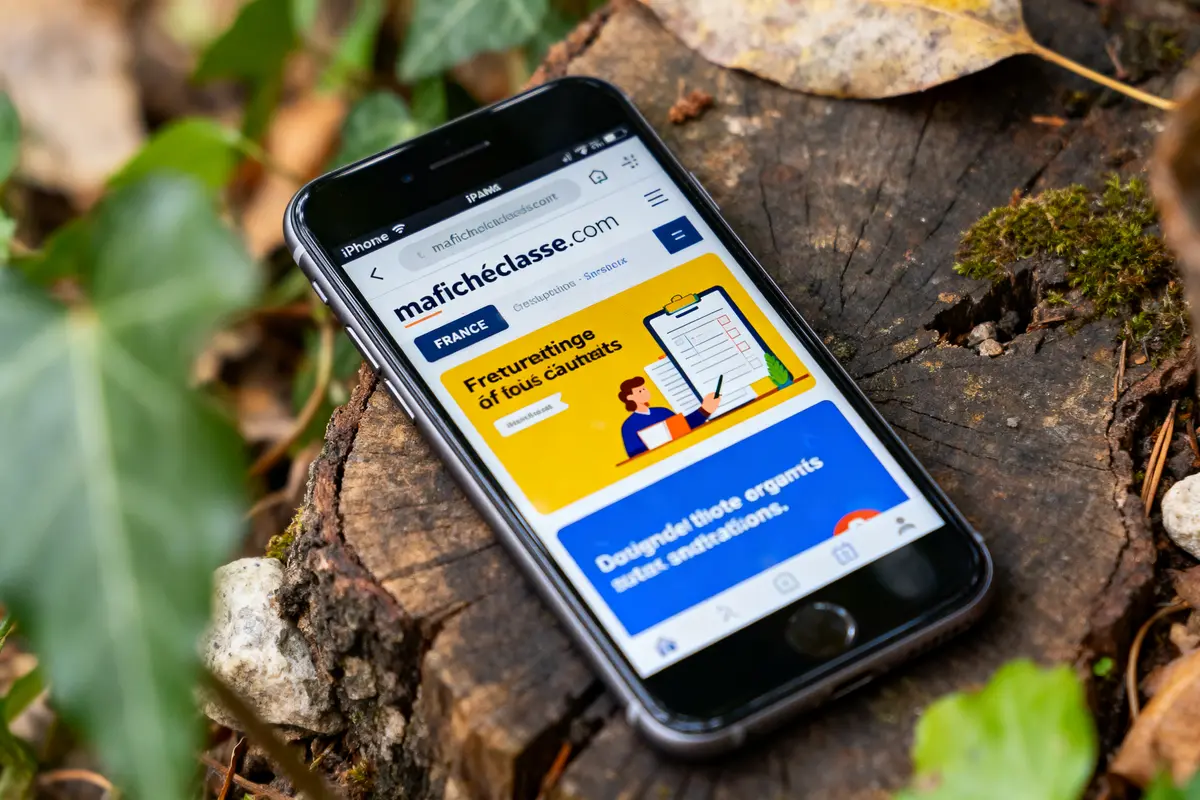 Smartphone sur une souche d'arbre affichant la page web "mafichedeclasse.com" avec des plantes autour.