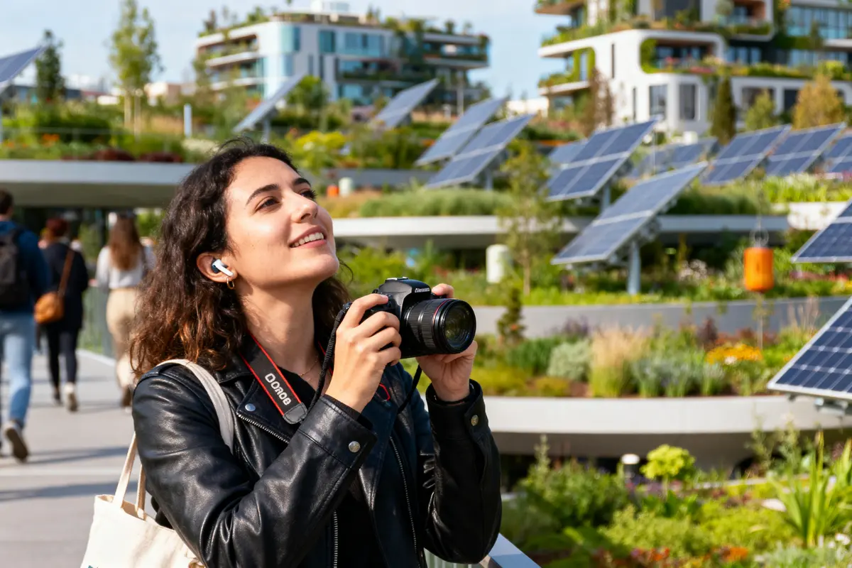 Jeune femme photographie jardin urbain avec panneaux solaires, écouteurs et appareil photo, bâtiments modernes en arrière-plan.